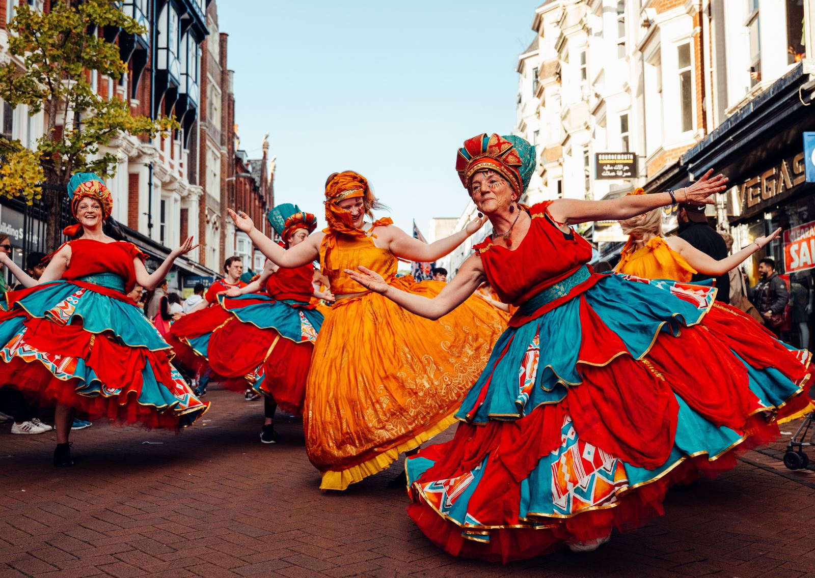 Three ladies dressed in bright colourful dresses smiling and dancing